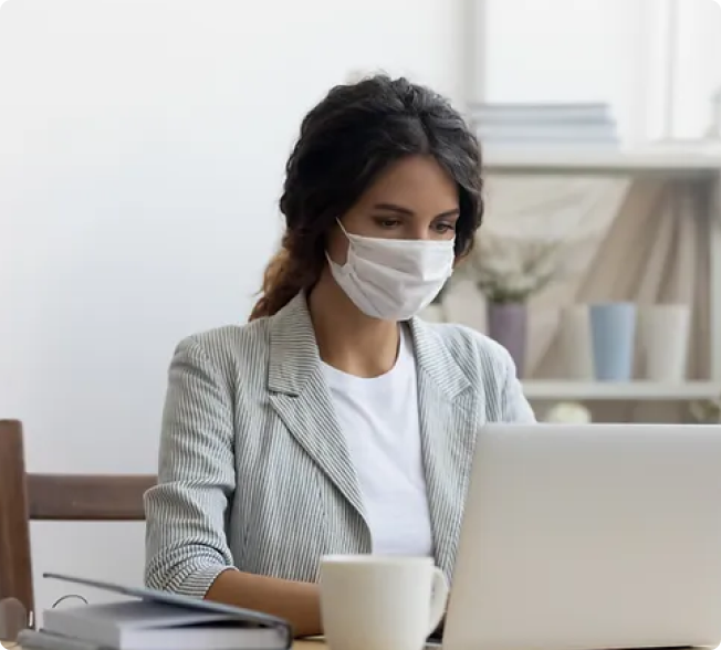 Professional woman working on a laptop while wearing a mask, representing remote work.